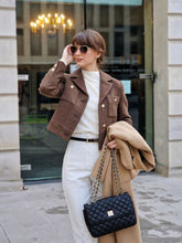 A lady wears a brown jacket and white pants.